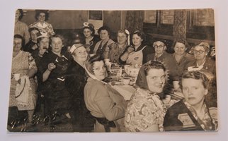 Sepia photo of a group of women sitting at a table with food on it, posing for the camera