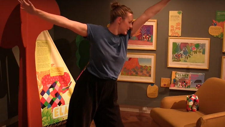Woman dancing in the Elmer exhibition with paintings and drawings around