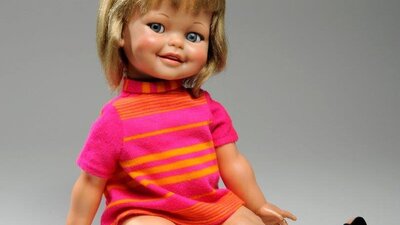 A Doll in a seated position wearing a pink and orange top