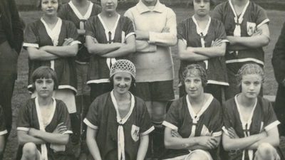A women's football team, crouched on the ground, one of the ladies is holding a football 