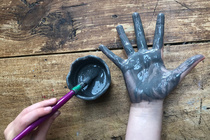 Grey paint pot with purple paint brush. Somebody has painted the palm of their hand grey