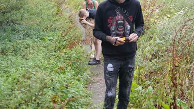 Two people walk along a narrow path through dense greenery