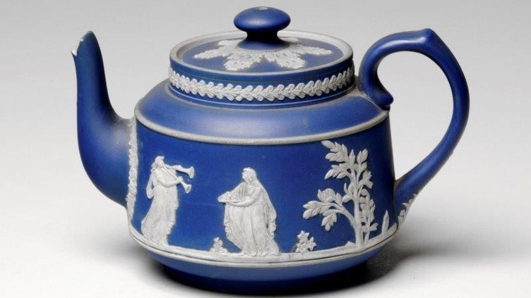 An ornate blue tea pot with white decorations of figures and plants