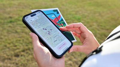 Close-up of hands holding a smartphone and pamphlet; phone displays the ARTQuest app with colorful art-themed graphics