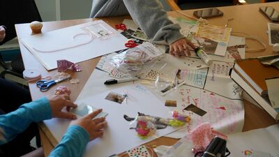 hildren sit around a table, drawing and writing on large sheets of paper