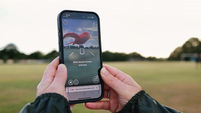 Person using a smartphone outdoors with an AR app showing a red bird over a nature scene