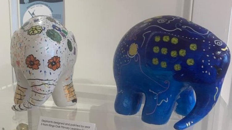 Two small ceramic elephants, one blue and one white on display in a glass cabinet