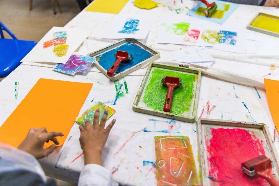 A child's hands over a table with paint rollers and colourful printed patterns