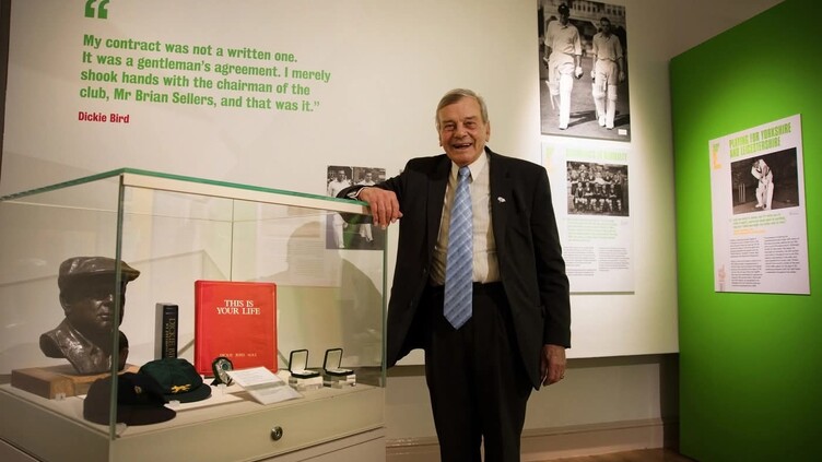 Dickie Bird in the exhibition space stood next to case containing memorabilia and his This is Your Life folder