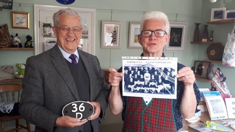 Ken and Ian in the Darield Museum shop, Ken is holding a plaque and Ian is showing to the camera a picture of Barnsley FC