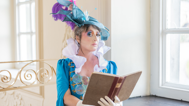 Woman dressed as Lady Wortley in a blue dress and hat reading a large old fashioned book