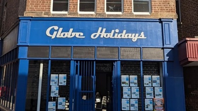 A blue storefront with the sign "Globe Holidays" in white letters. The windows display multiple posters, and the building is made of red brick.