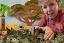 Woman sitting with a model jungle with trees and monkeys in it
