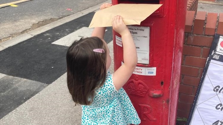 Little girl posting letter through letterbox