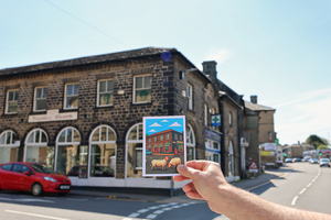 Person holding a cartoon-style illustration of a stone building in front of the actual building