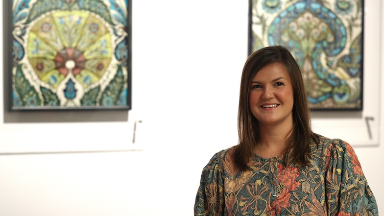 Woman stood in front of two paintings in an exhibition, smiling at the camera