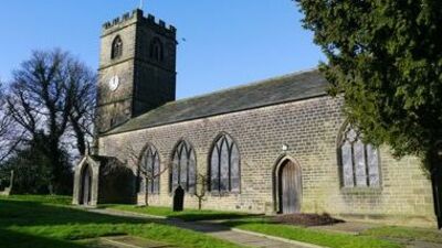 A stone church with a square clock tower and arched windows stands under a clear blue sky, surrounded by grass, trees, and a pathway.