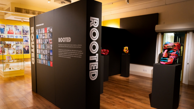 A view of the exhibition on the back wall slightly out of view is a wall of photo, there is a colourful carved head sculpture to the right