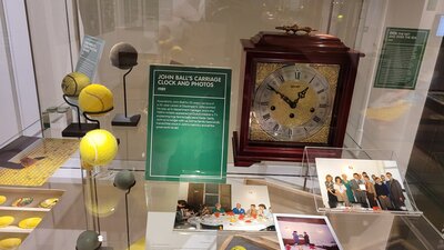 One of the cases in the exhibition which includes a clock, tennis balls and a several photos