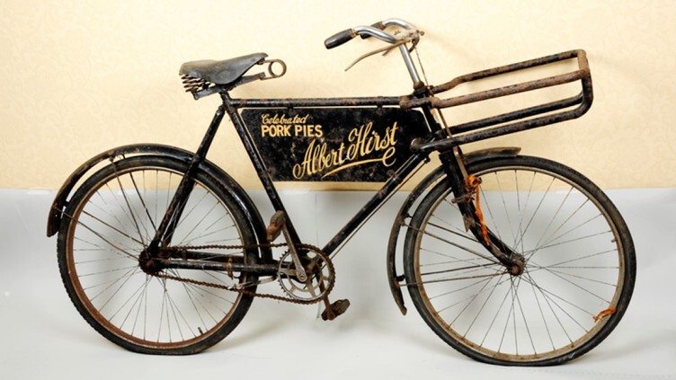 An old fashioned black bicycle with 'Albert Hirst - Celebrated pork pies' written on it in yellow writing